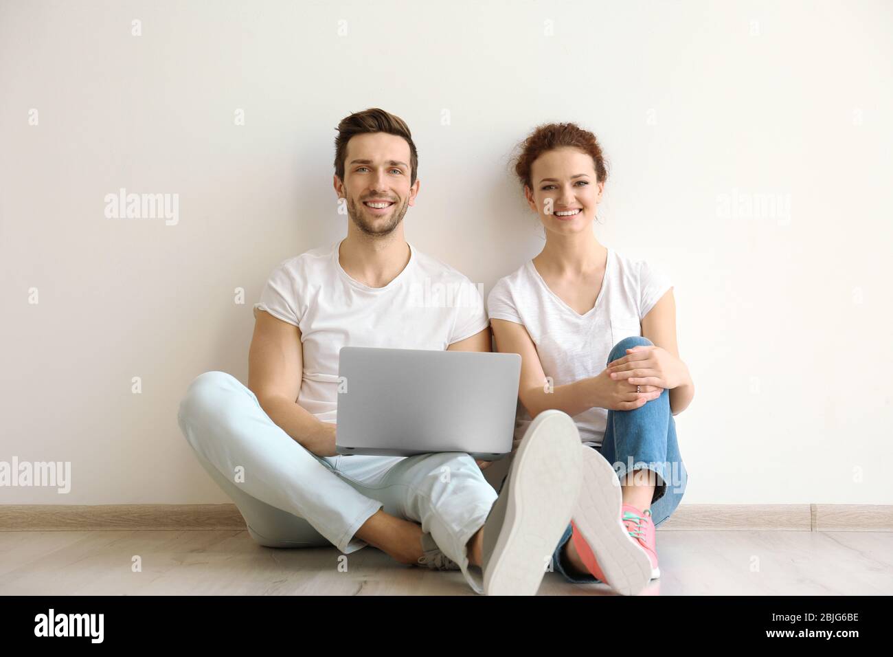 Happy young couple with laptop sitting on floor at home Stock Photo - Alamy