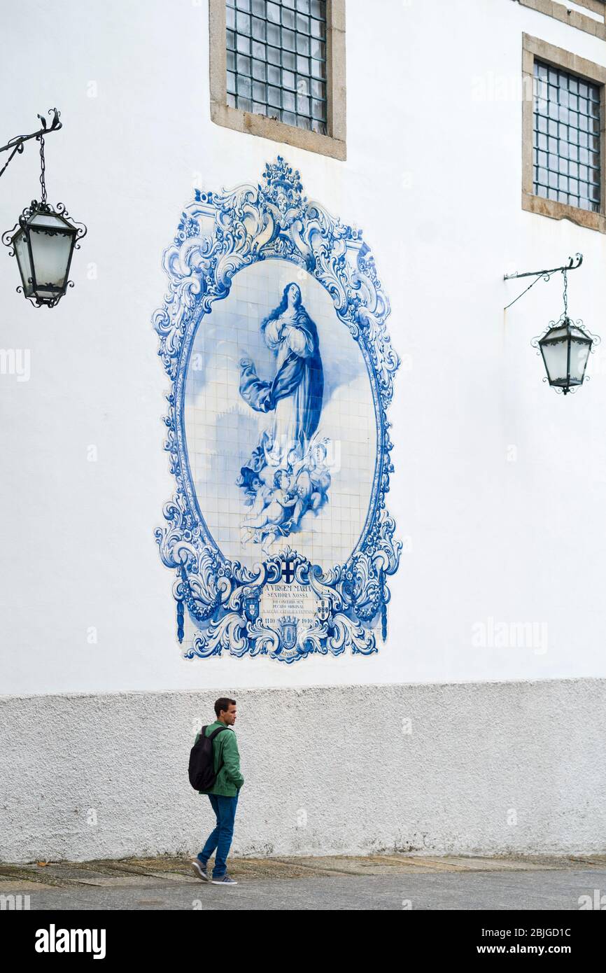 Young man passing blue and white azulejos ceramic tiles of Convent Church of Carmo in Guimares in Northern Portugal Stock Photo