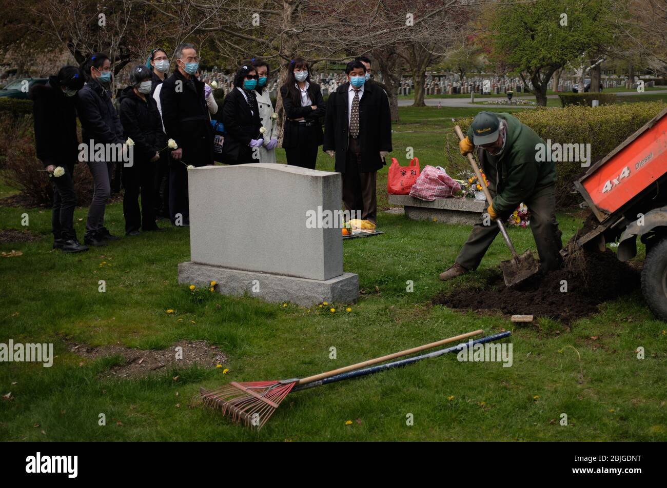 Everett, Massachusetts, USA. 28th Apr, 2020. The COVID-19, Corona Virus in Massachusetts is the third worst hit state in America. The Woodlawn Cemetery in Everett, MA is doing 3x the normal amount of funerals. Family with masks and gloves watches men fill in a grave during a traditional Chinese funeral. Credit: Allison Dinner/ZUMA Wire/Alamy Live News Stock Photo