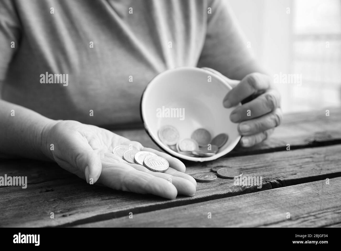 Senior woman sitting at table with bowl and coins, closeup. Poverty concept Stock Photo