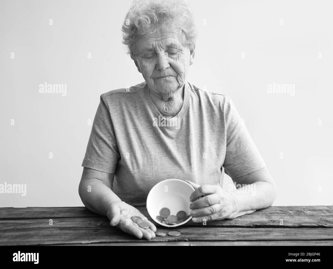 Senior woman sitting at table with bowl and coins. Poverty concept Stock Photo
