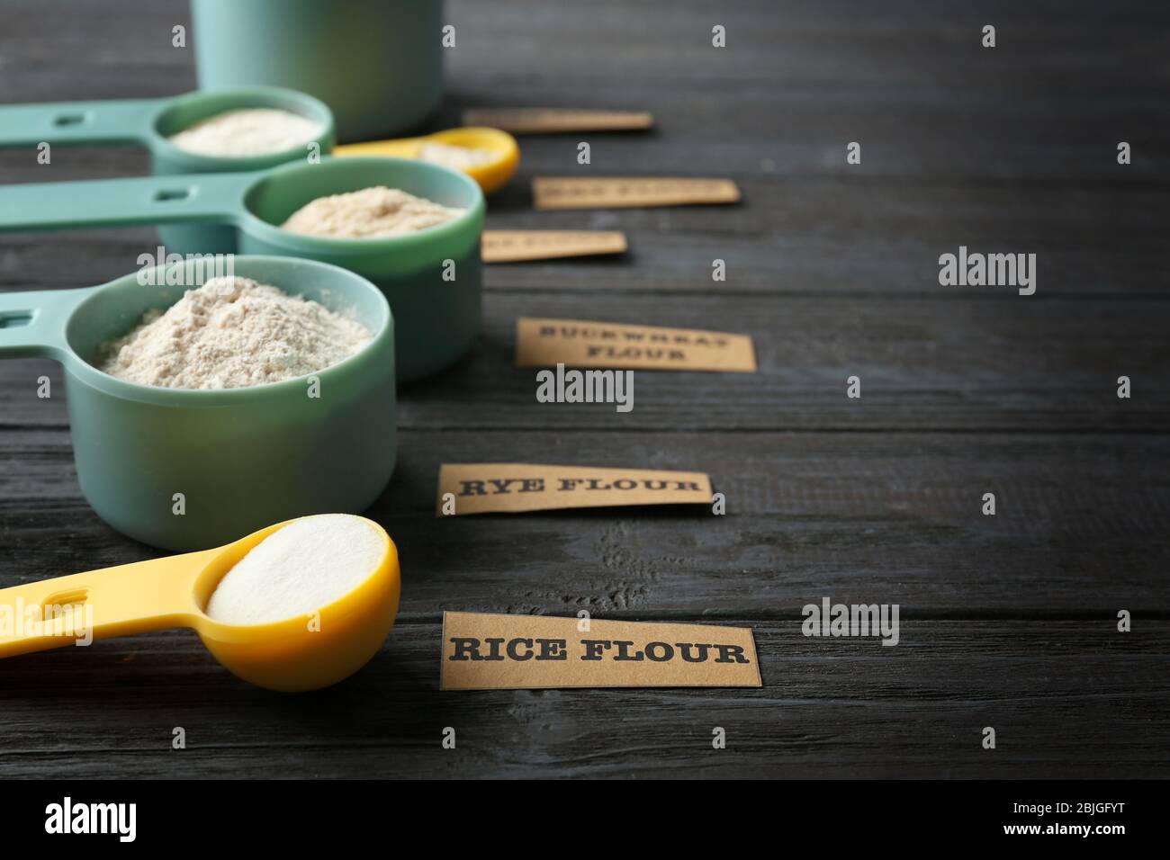 Measuring scoops with different types of flour on wooden background