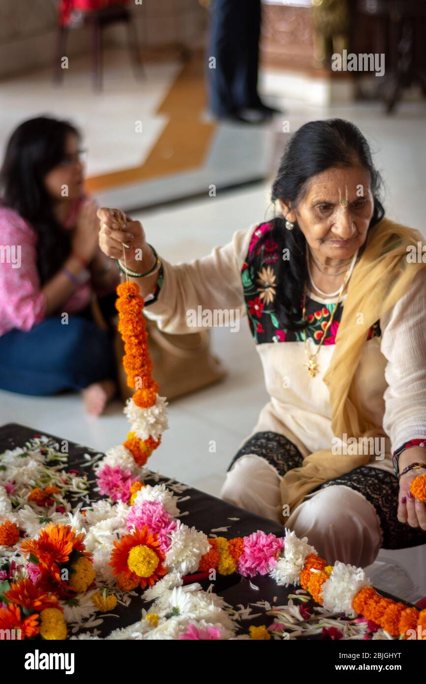Delhi / India - October 2, 2019: Hindu women weaving flower garlands, decorative wreath of flowers, at ISKCON Delhi Hindu temple of Lord Krishna, New Stock Photo