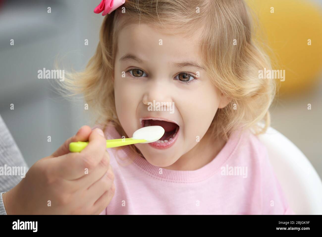 Mother feeding cute little girl with yogurt at home, closeup Stock