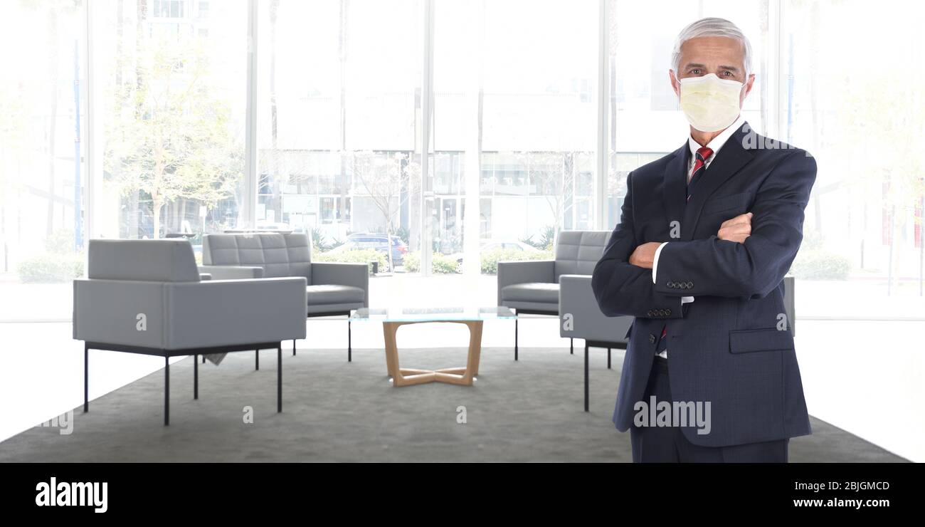 Businessman standing in empty office without customers or employees wearing his COVID-19 mask practicing social distancing. Wide format with copy spac Stock Photo