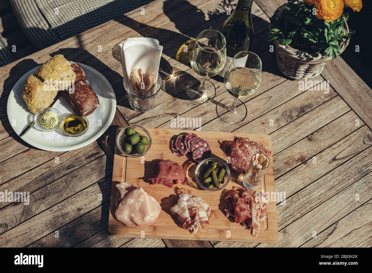 Charcuterie board served with white wine outdoors.  A platter of ham & bacon slices with pickles on a wooden board Stock Photo