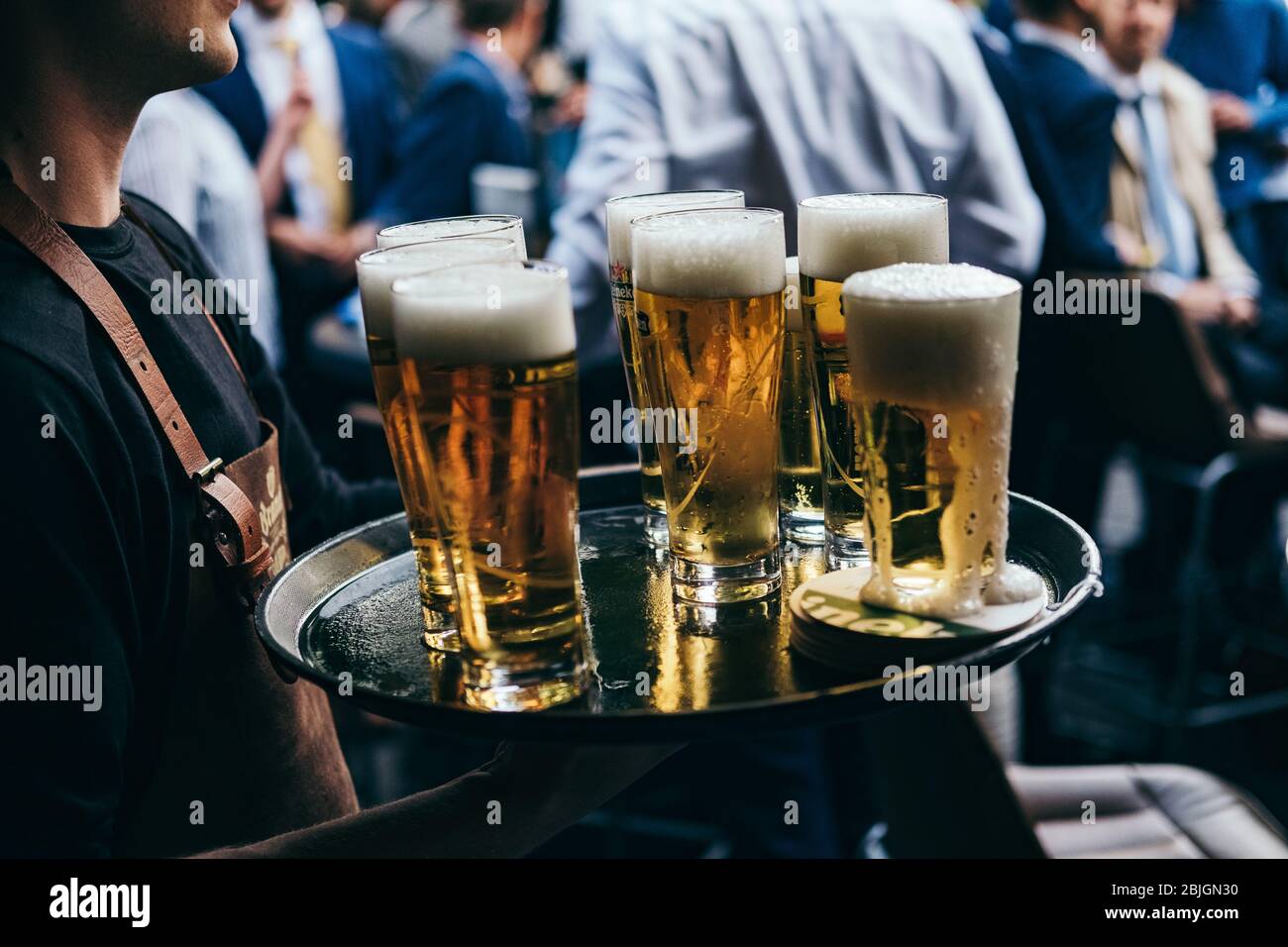waiter carries tray full of glasses of beer to customers at outdoor bar or pub Stock Photo