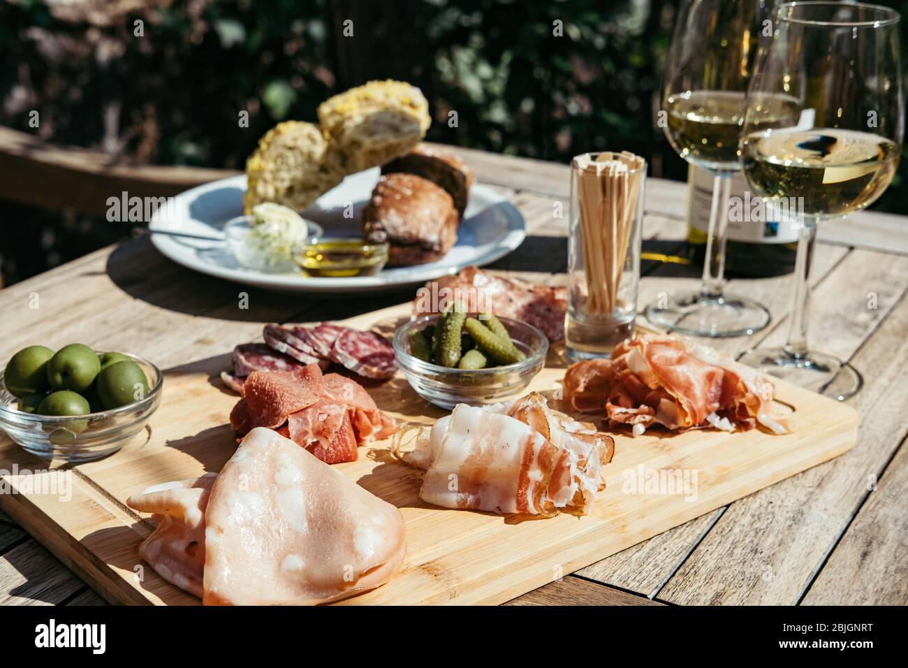 Two Glasses and Bottle of White Wine with Gourmet Charcuterie Board on round Marble Table. Garden Party. Stock Photo