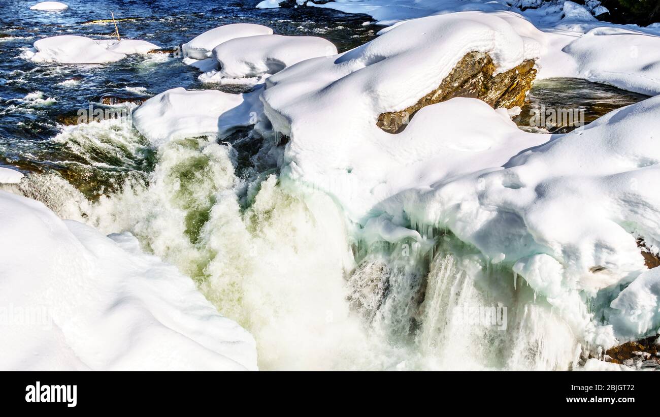 Water of the Murtle River tumbles over the edge of the partly frozen Mushbowl Falls in the Cariboo Mountains of Wells Gray Provincial Park Stock Photo