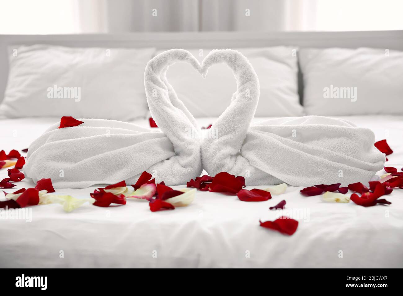 Two towel swans and rose petals on bed in light hotel room Stock Photo