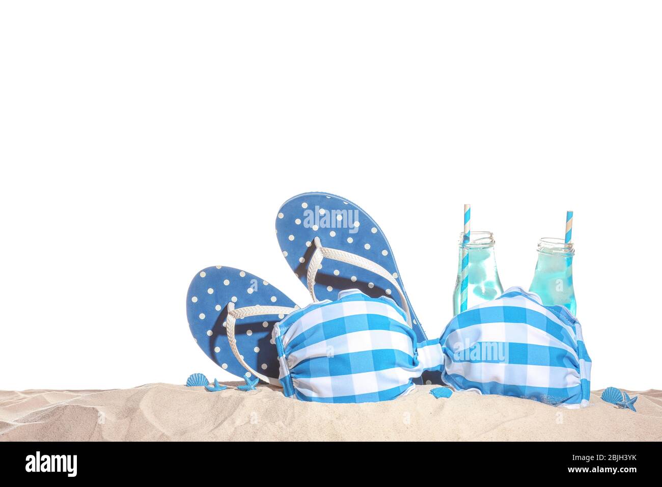 Swimsuit, flip-flops and cold drinks on sand against white background