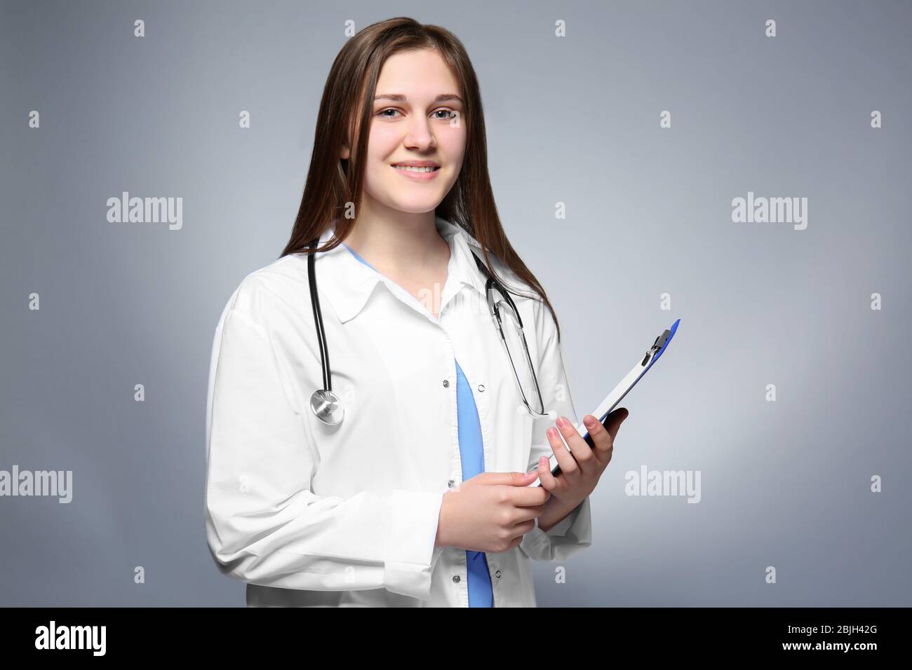Young female intern with clipboard on grey background Stock Photo