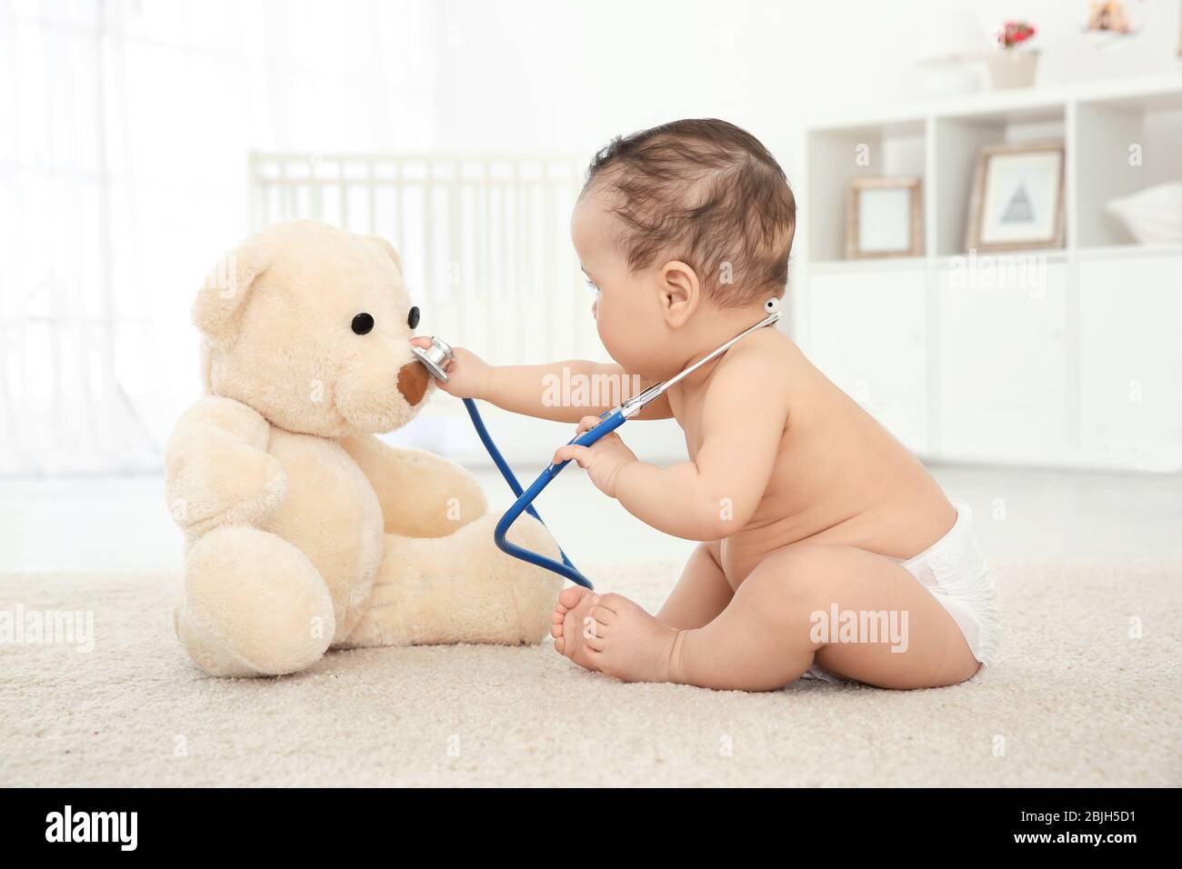 Cute little baby with stethoscope and toy bear playing at home ...