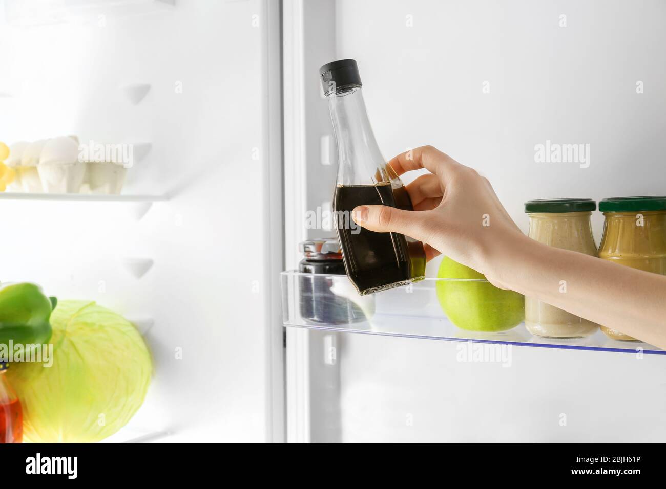 Hand of young woman taking bottle with soy sauce from fridge Stock