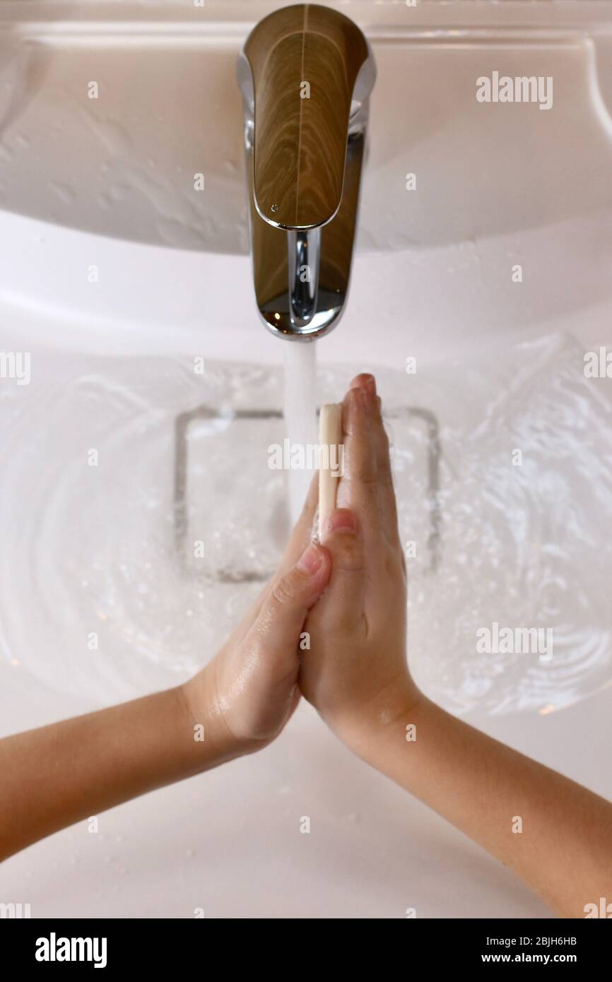 The child learns to wash his hands with a bar of soap, with water in the sink. Stock Photo