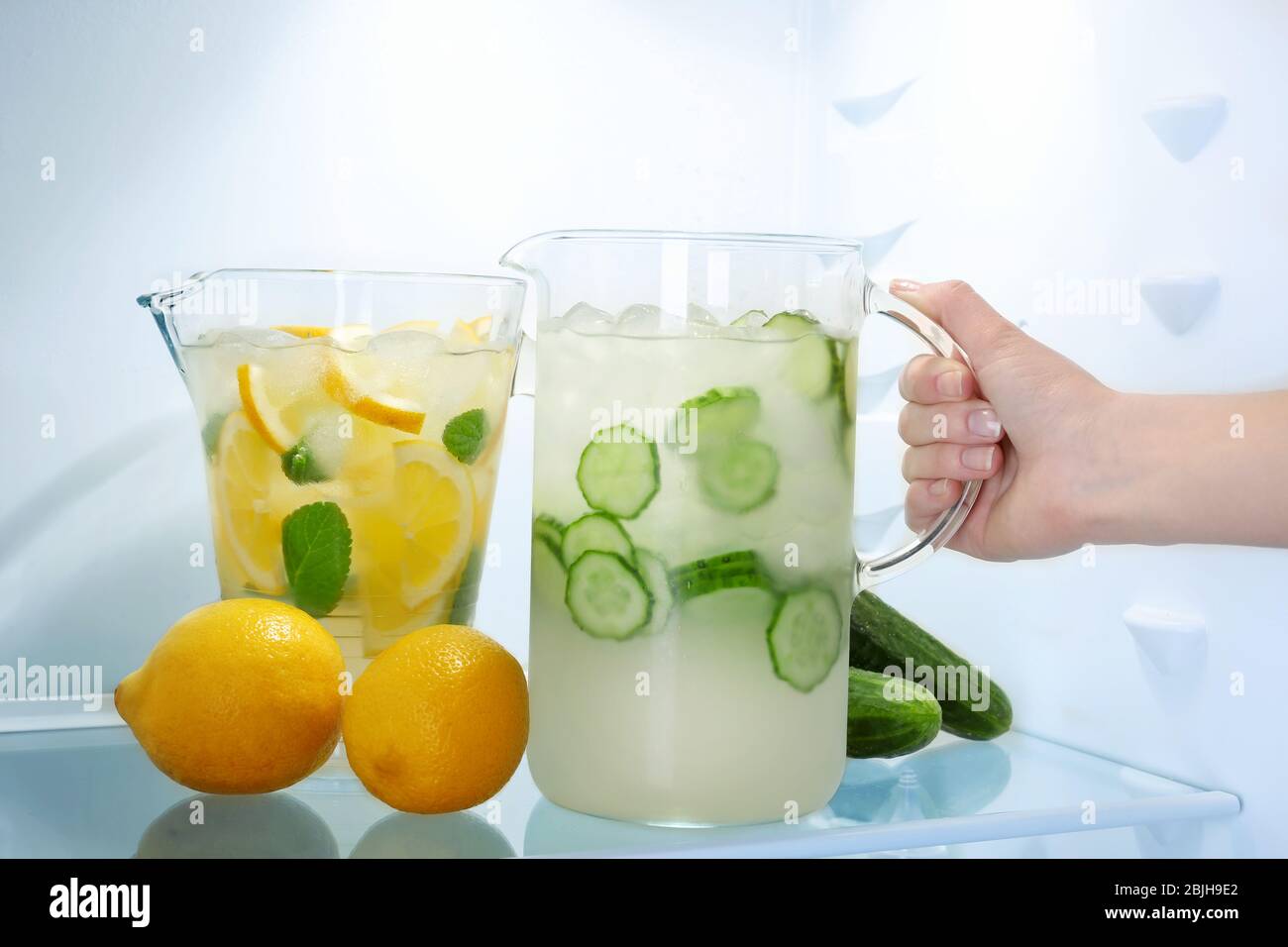 Female hand taking jug of cucumber lemonade from fridge Stock Photo