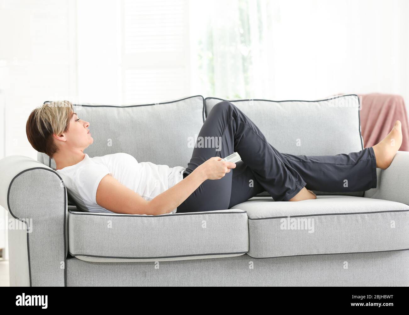 Mature woman watching TV while lying on sofa at home. Sedentary lifestyle concept Stock Photo