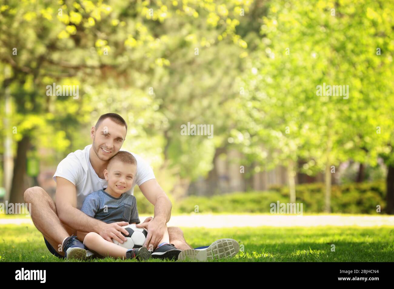 Father and son with soccer ball sitting on green grass in park Stock ...