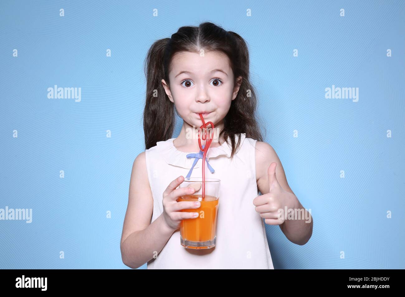 Cute little girl drinking juice on color background Stock Photo - Alamy