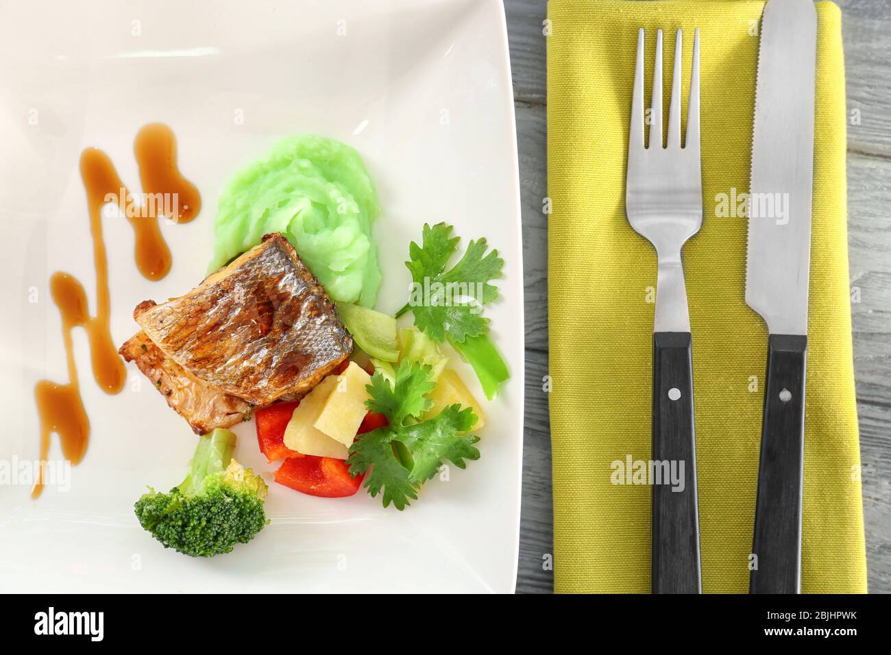 Plate with delicious fish, sauce, vegetables and cutlery on table Stock