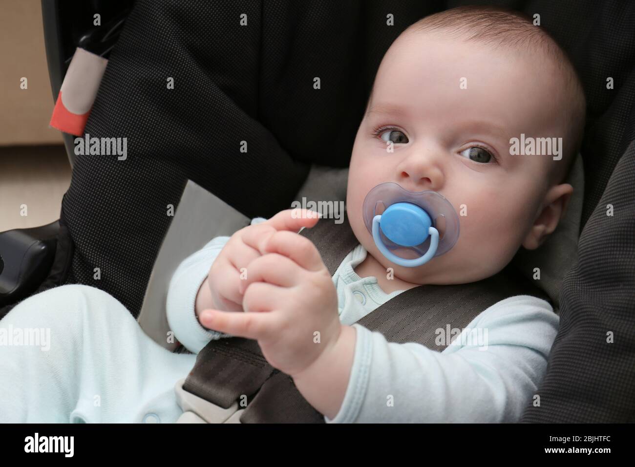 Cute baby boy with pacifier sitting in safety car seat Stock Photo Alamy