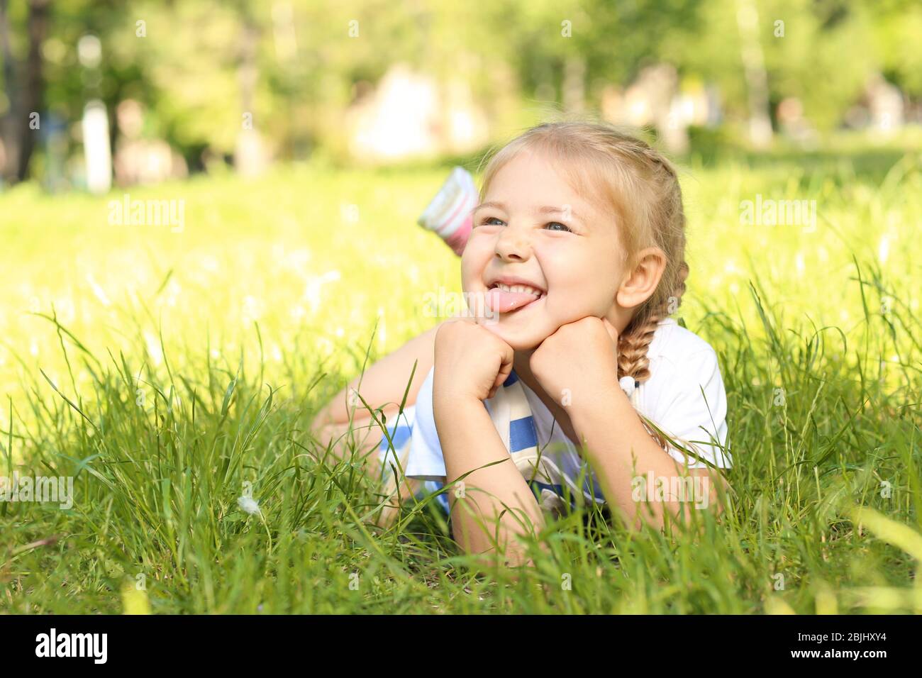 Cute little girl lying on green grass in park Stock Photo - Alamy