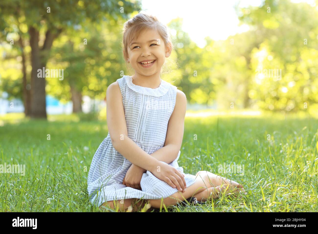 Cute little girl sitting on green grass in park Stock Photo - Alamy
