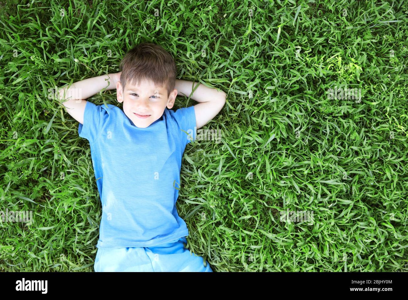 Cute little boy lying on green grass in park Stock Photo - Alamy