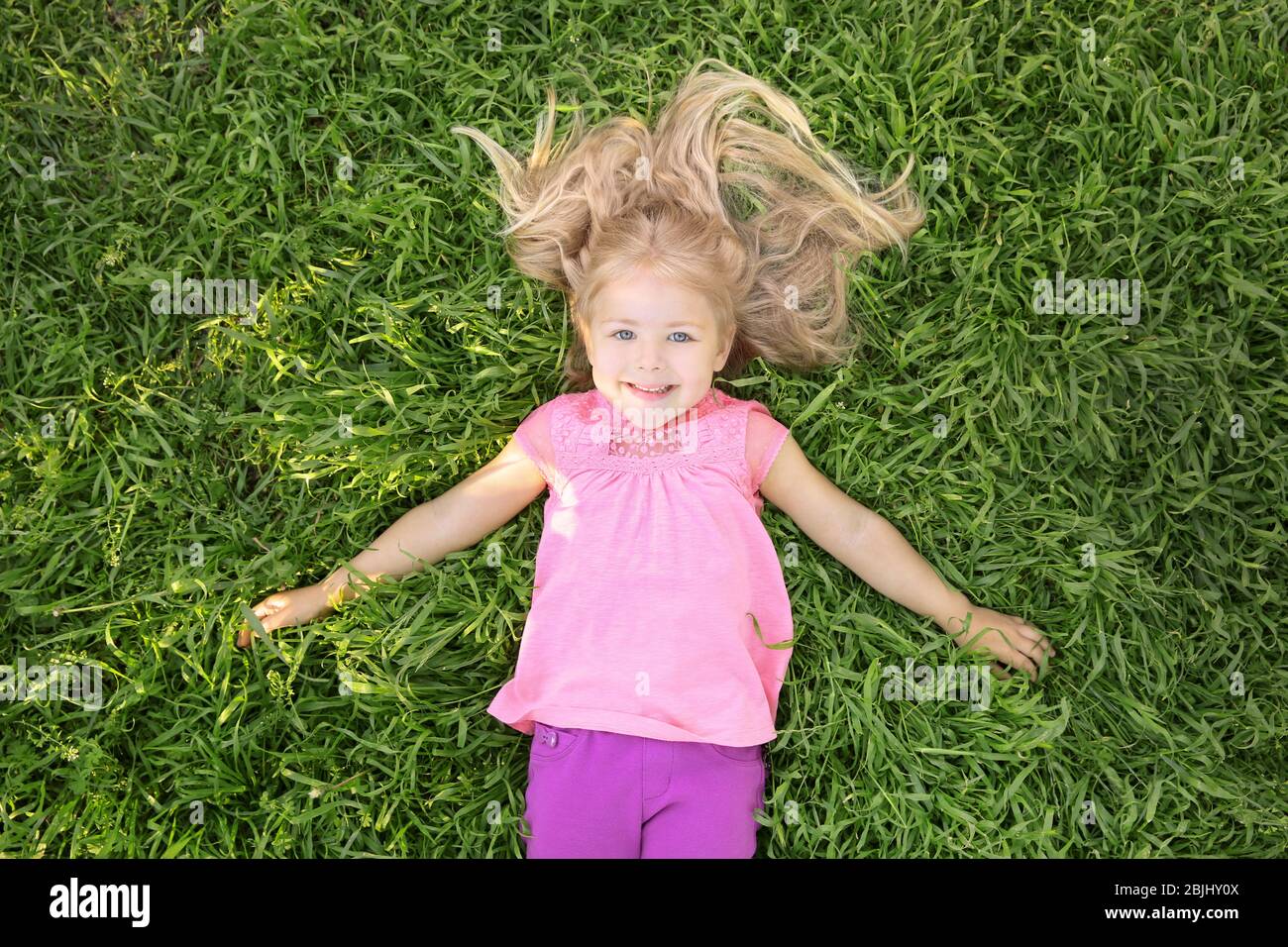 Cute little girl lying on green grass in park Stock Photo - Alamy