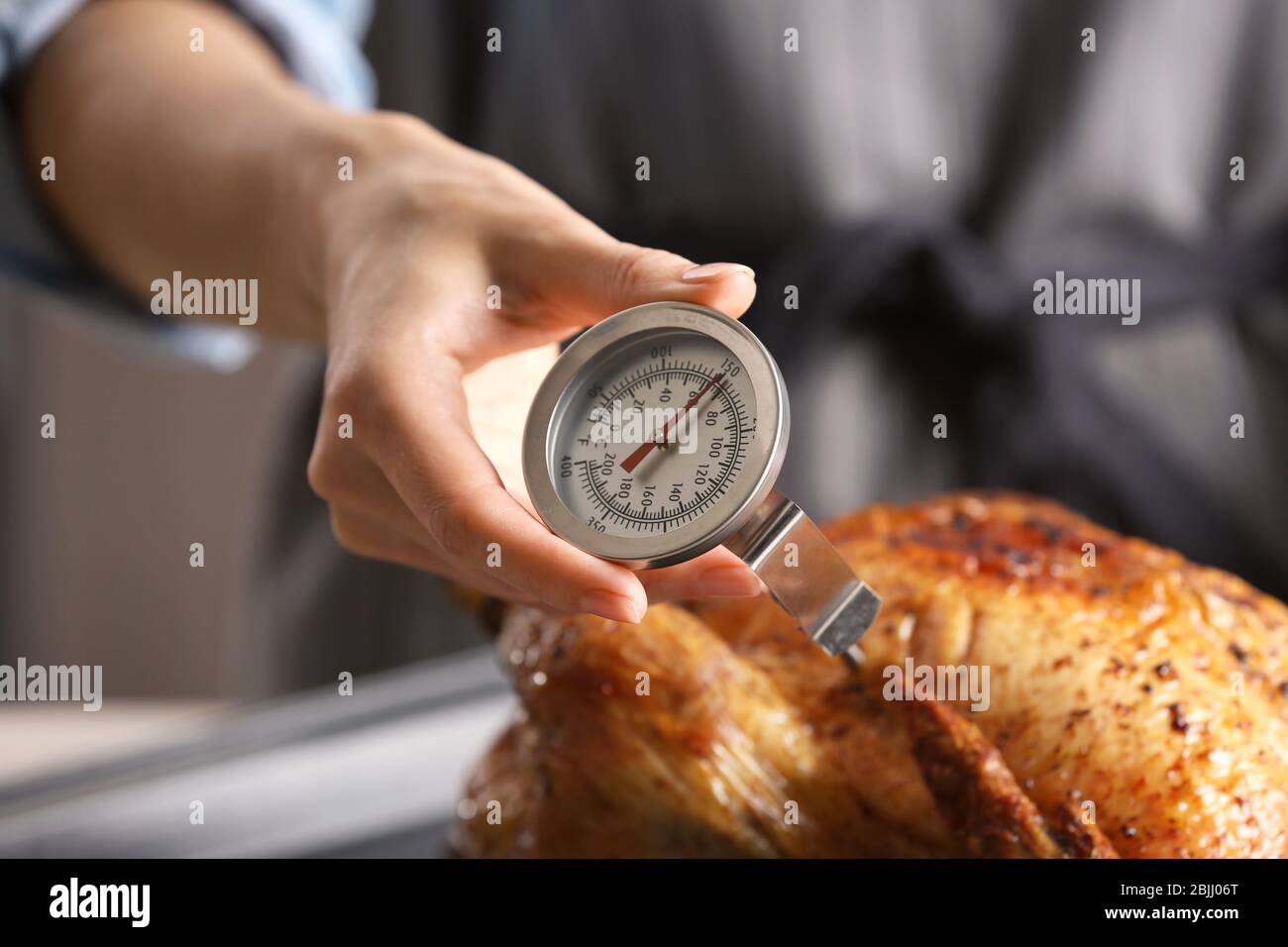 Young woman measuring temperature of whole roasted turkey with meat  thermometer Stock Photo