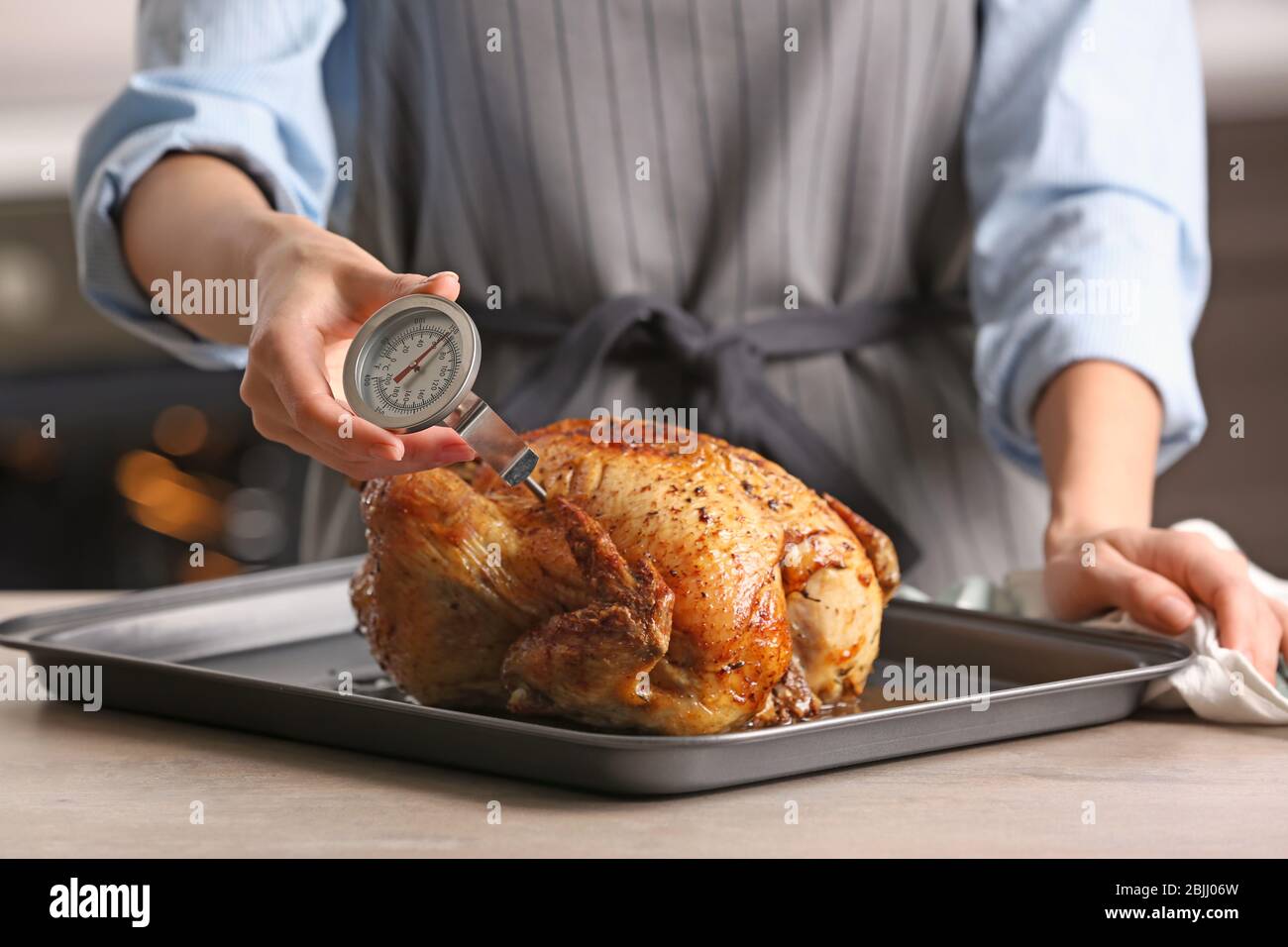 Young woman measuring temperature of whole roasted turkey with meat  thermometer Stock Photo