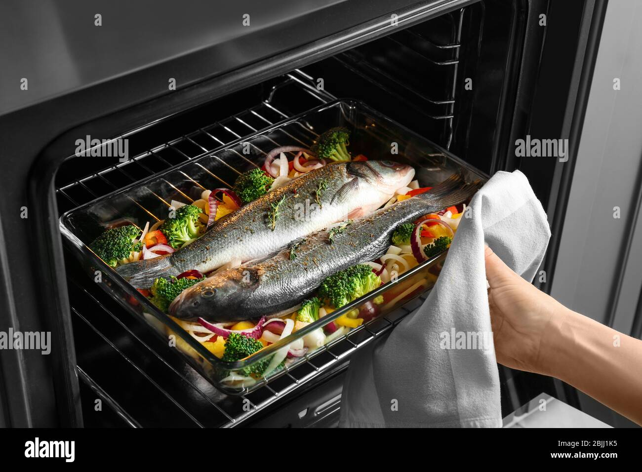 Woman putting baking tray with fish and vegetables into oven Stock Photo -  Alamy