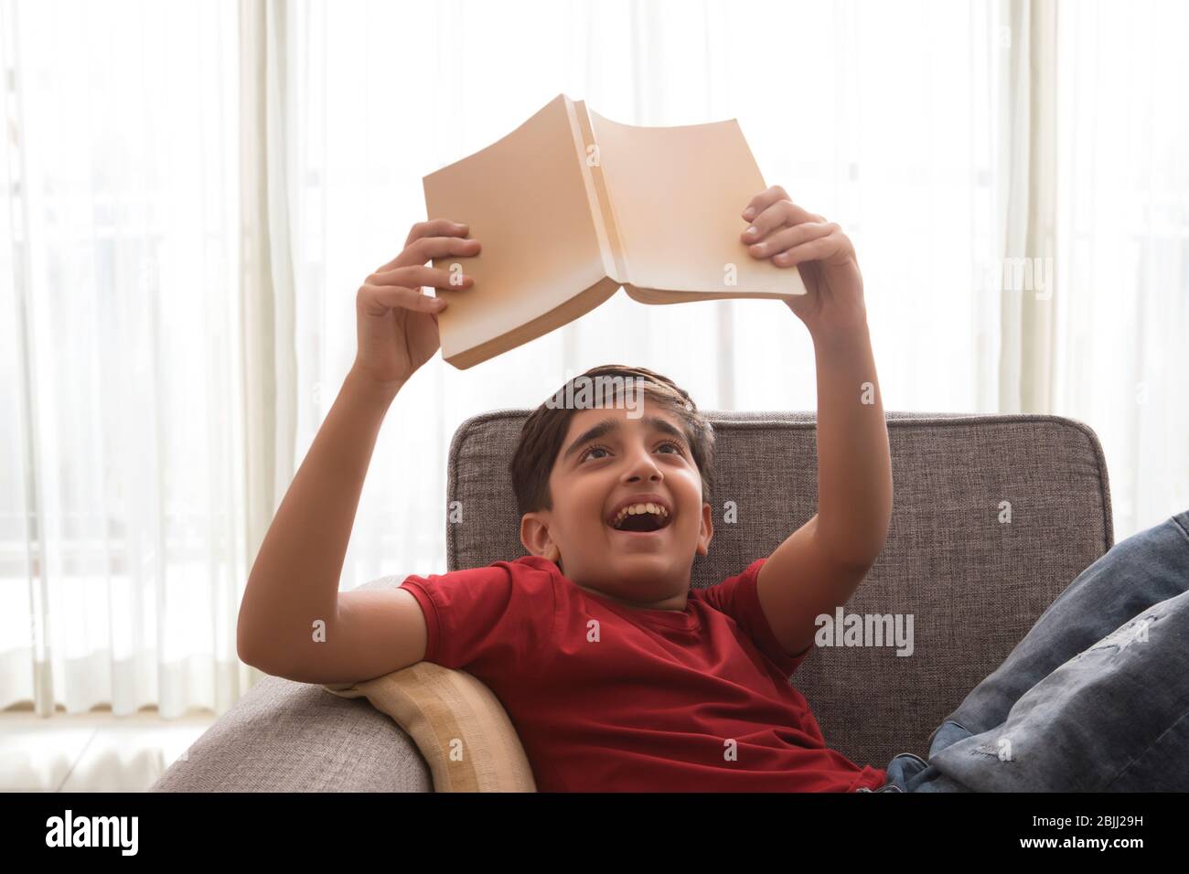 Portrait of a happy young boy lying on a couch and reading a book. (Children) Stock Photo