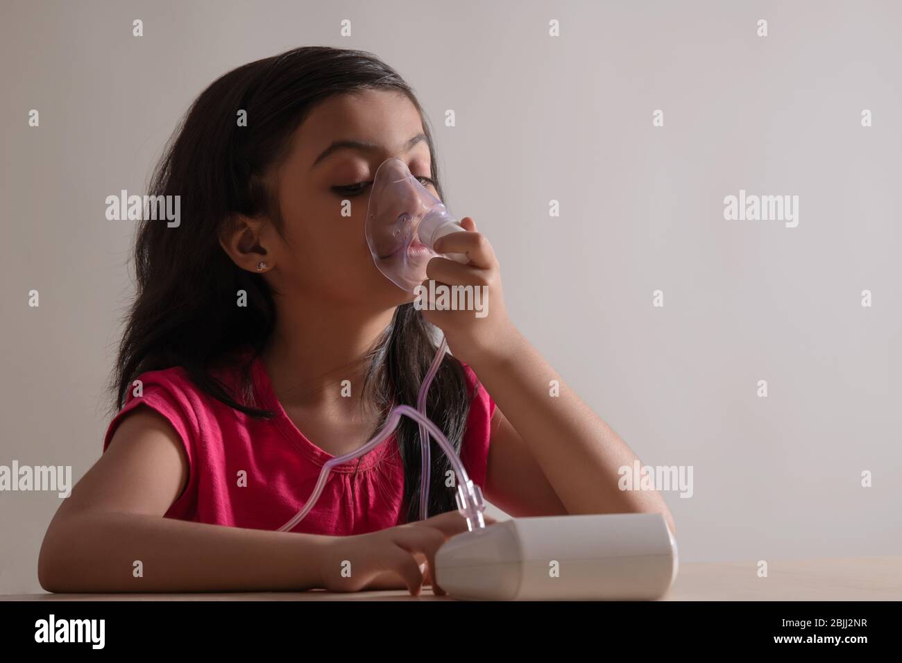 Young girl sitting and inhaling through a nebuliser at home. (Children) Stock Photo