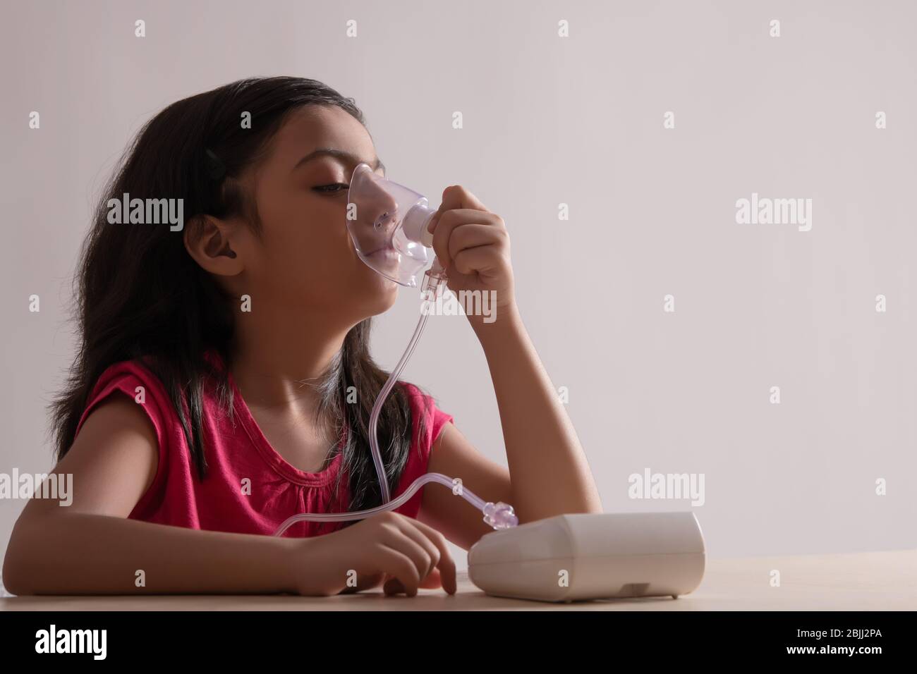 Young girl sitting and inhaling through a nebuliser at home. (Children) Stock Photo