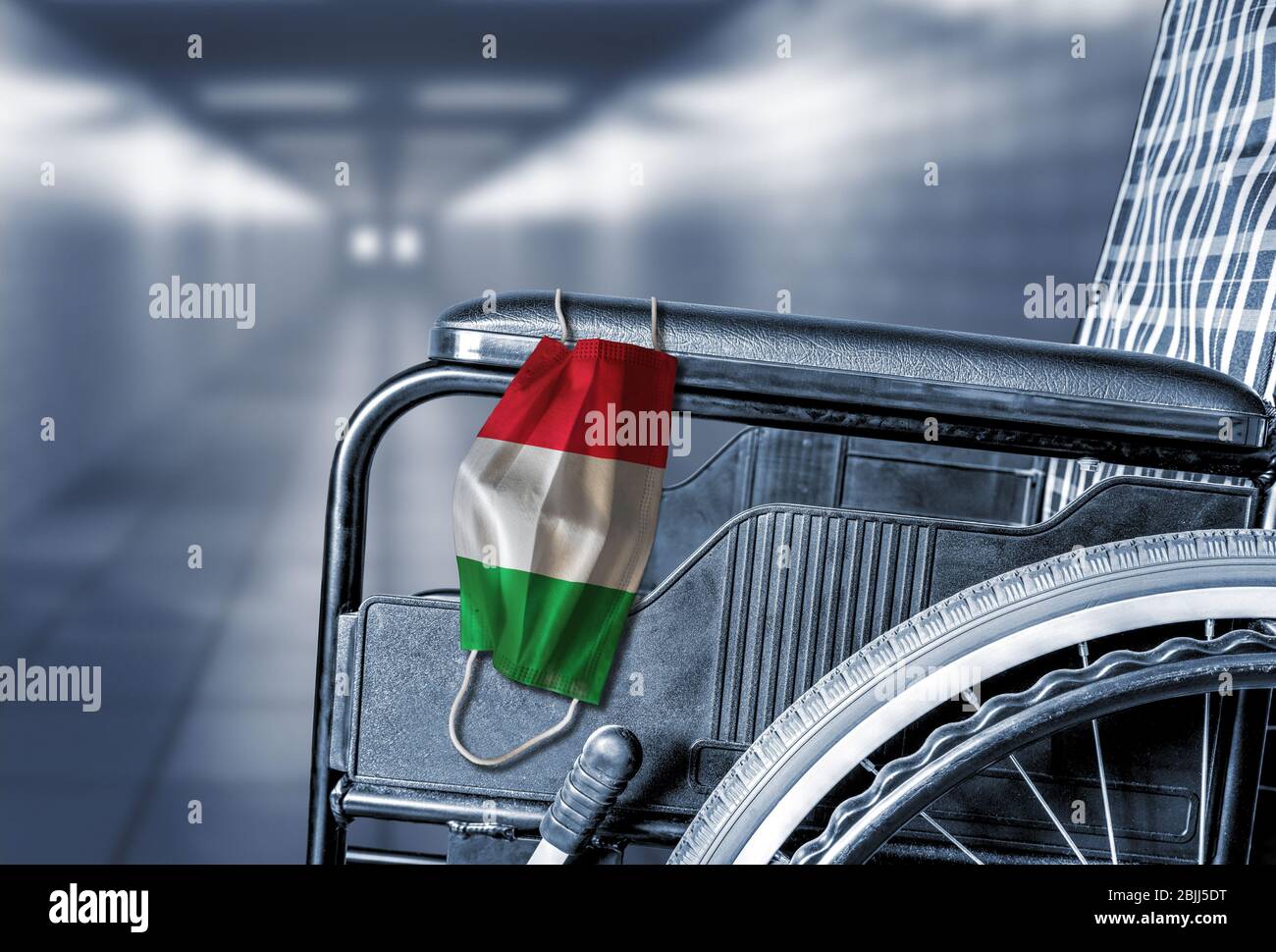 Flag of Italy on face mask hanging on empty wheelchair in hallway of Italian hospital or retirement nursing care home with copy space. Concept of heal Stock Photo