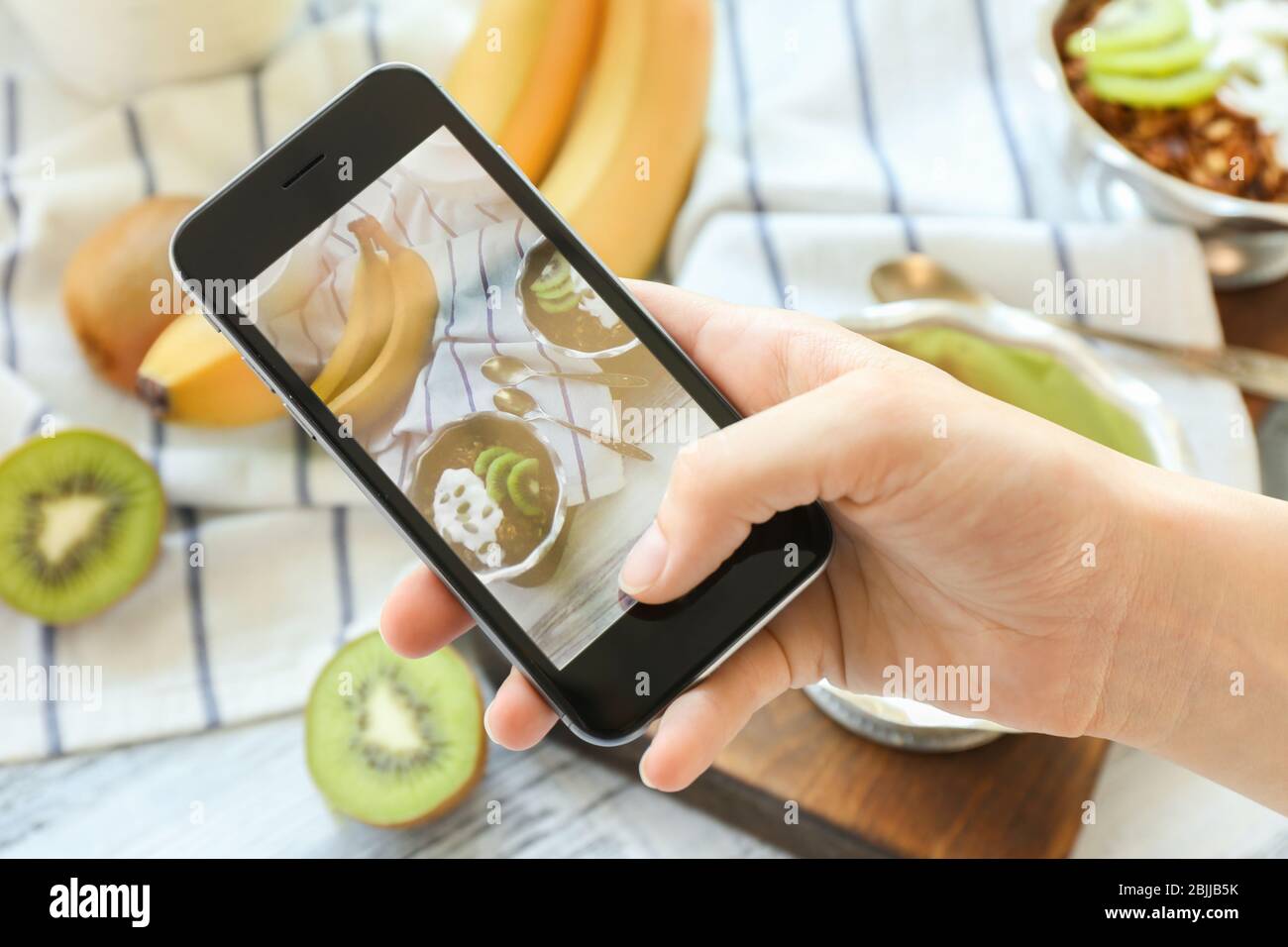 Young woman taking photo of delicious dessert in bowl with mobile phone ...