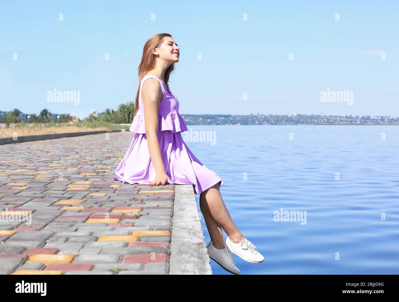 Beautiful young woman sitting on a riverbank Stock Photo - Alamy