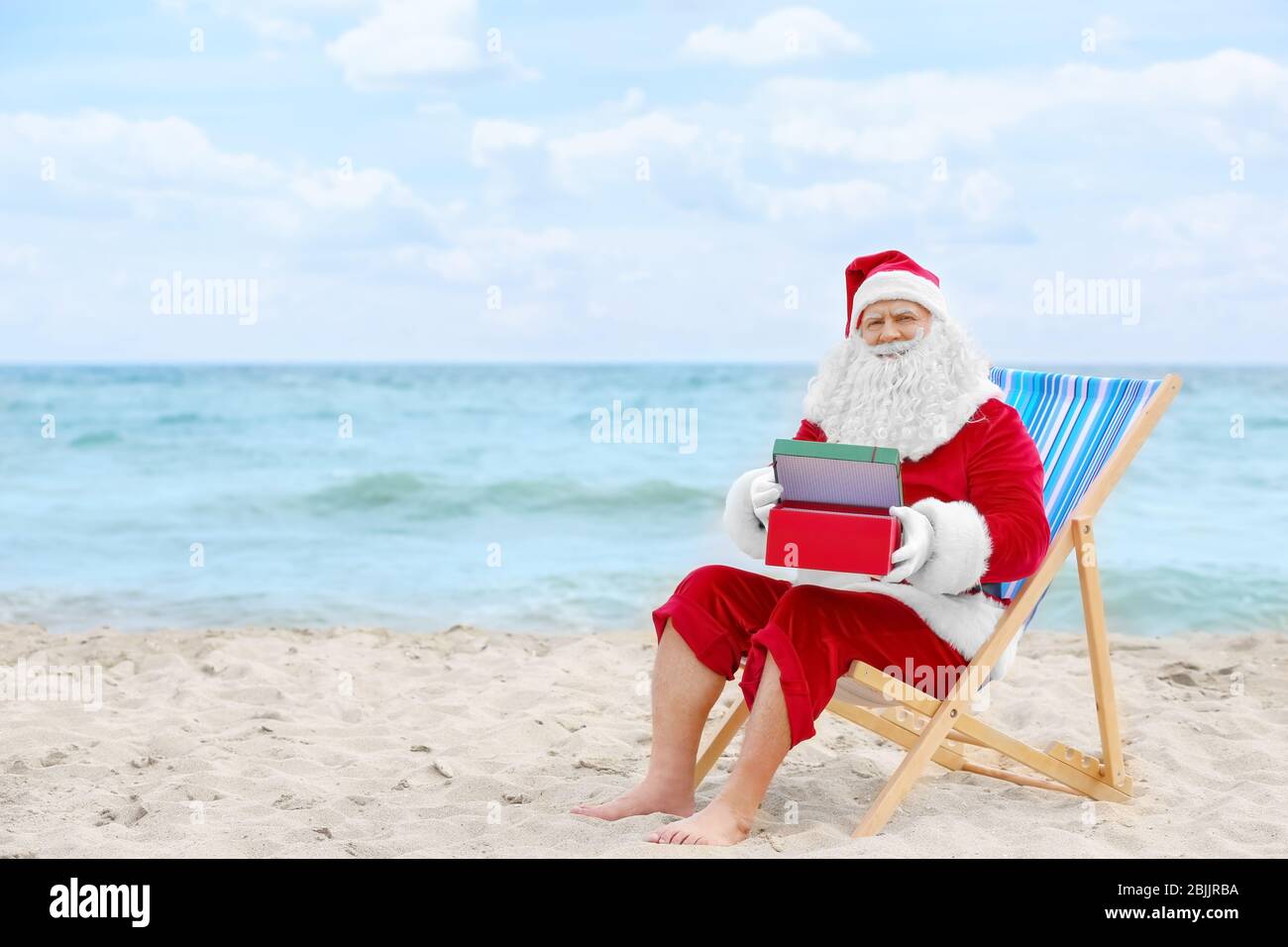 Authentic Santa Claus with gift box in deck chair on beach Stock Photo ...