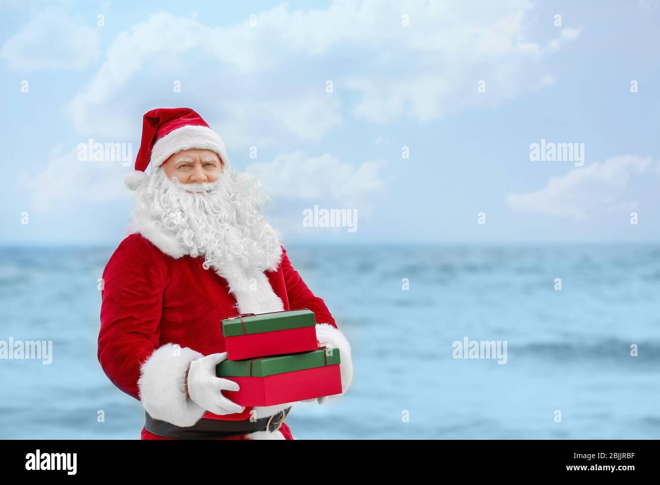Authentic Santa Claus holding gift boxes on sea background Stock Photo ...