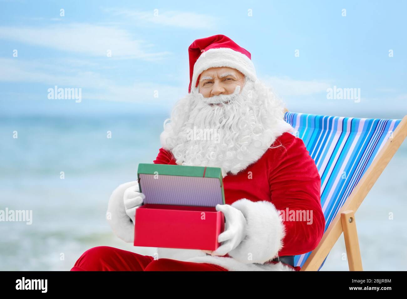 Authentic Santa Claus with gift box in deck chair on beach Stock Photo ...