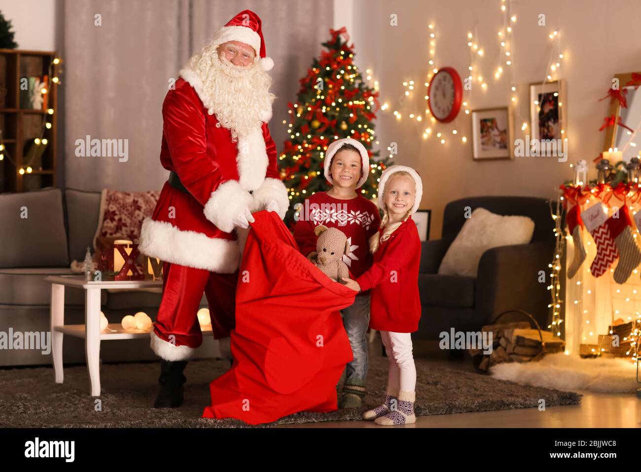 Santa Showing Presents To Cute Kids In Room With Beautiful Christmas santa-showing-presents-to-cute-kids-in-room-with-beautiful-christmas