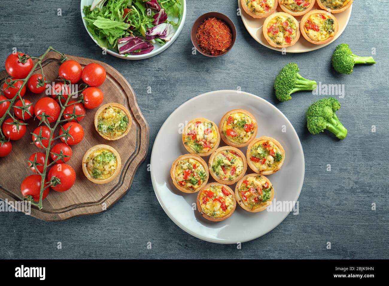 Composition with broccoli quiche tartlets and vegetables on table Stock Photo