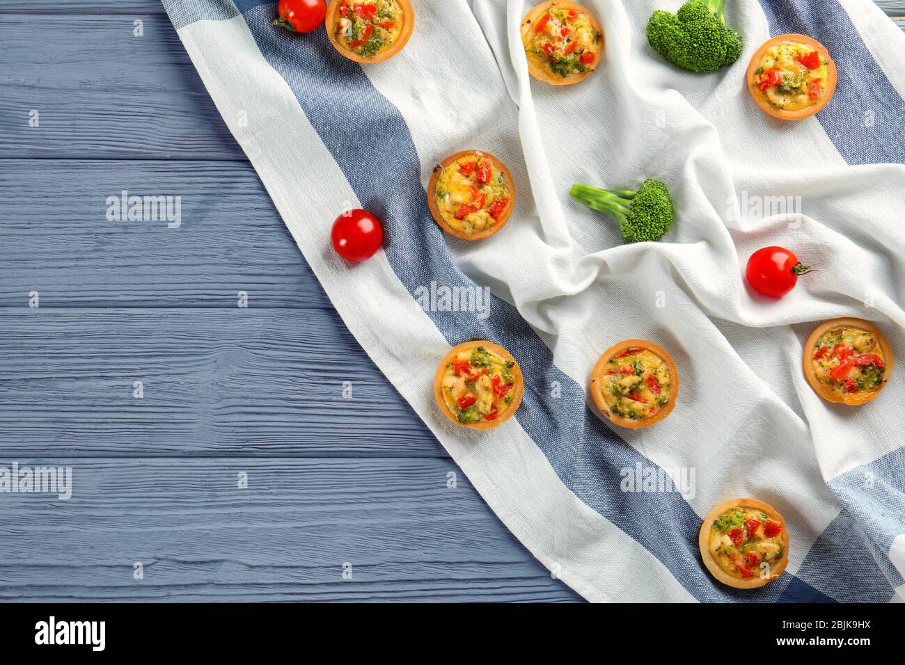 Composition with broccoli quiche tartlets and vegetables on table Stock Photo