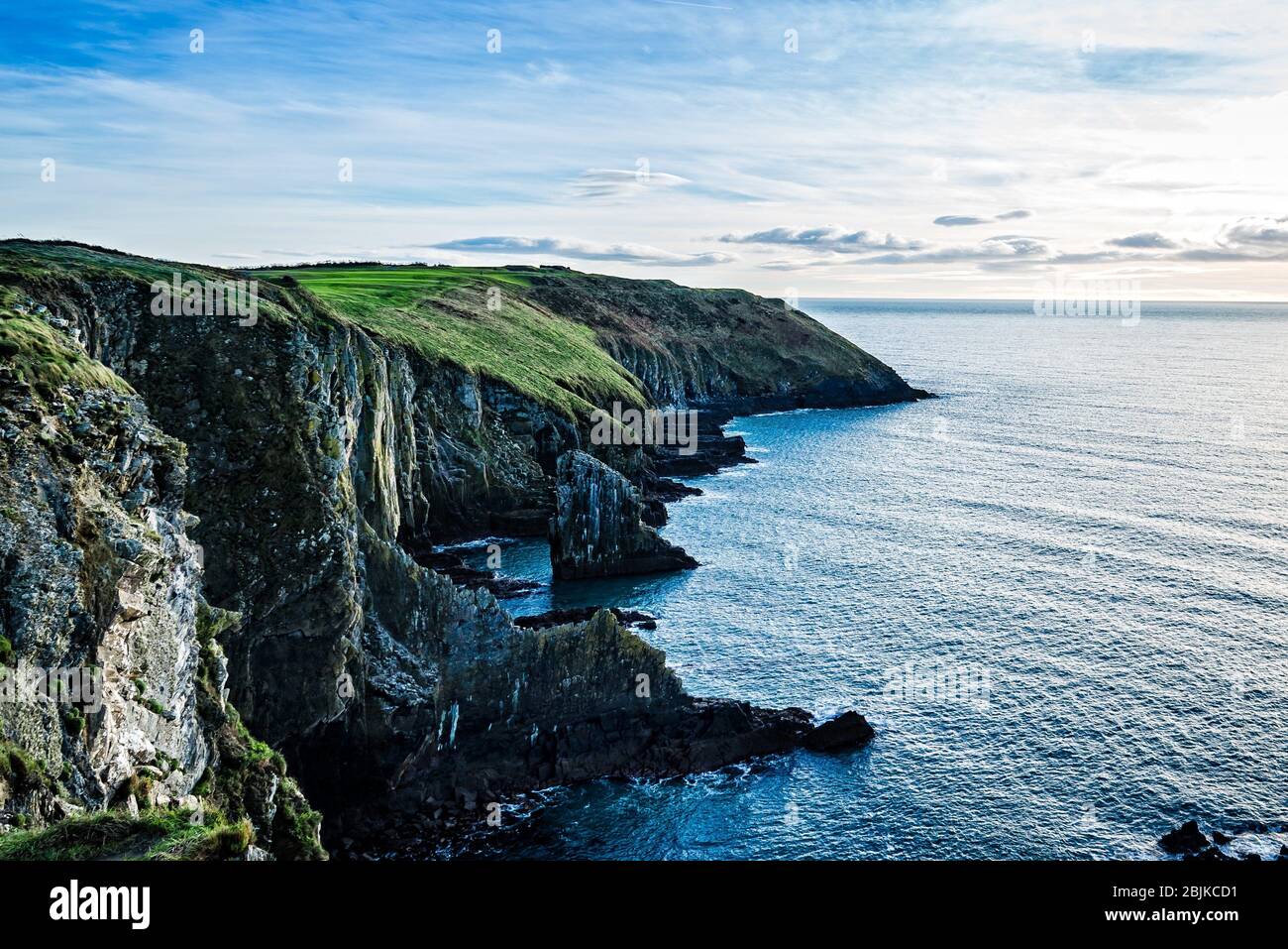 Scenic view of cliffs in Old Head of Kinsale peninsula in Ireland with green hills at sunset. Stock Photo