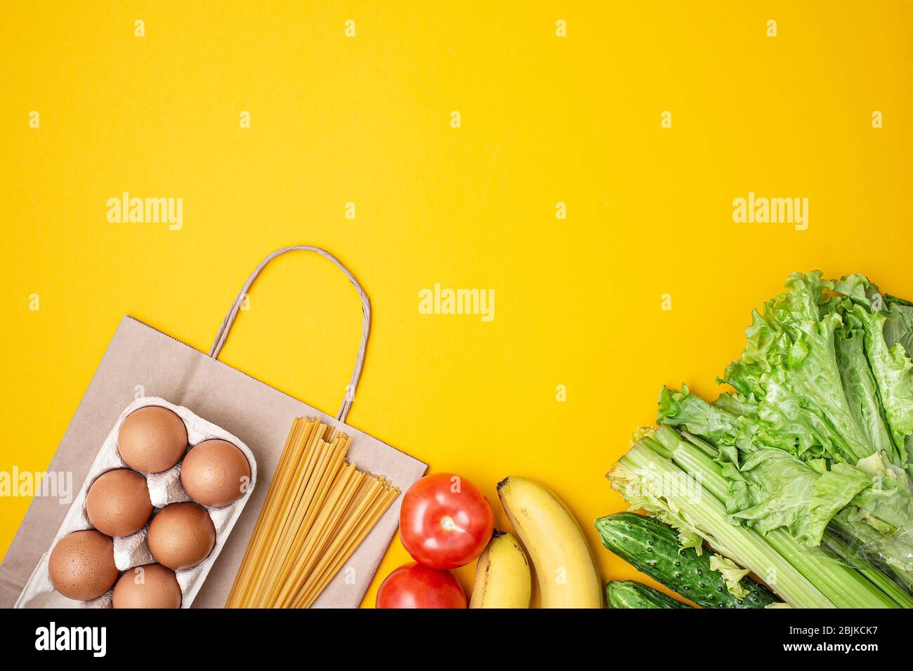 Paper bag with food, canned food, tomatoes, cucumbers, bananas on a yellow background. Donation, coronavirus quarantine. Food supplies for quarantine. Stock Photo