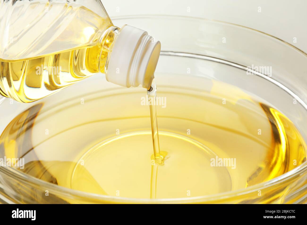 Pouring cooking oil from plastic bottle into glass bowl, closeup Stock
