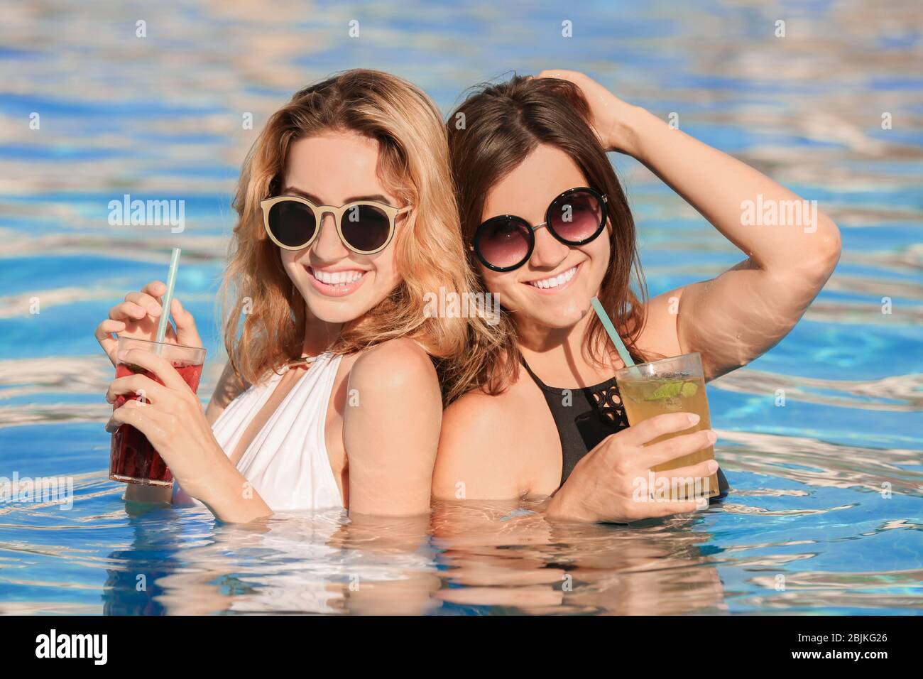 Two beautiful women with cocktails relaxing in pool Stock Photo