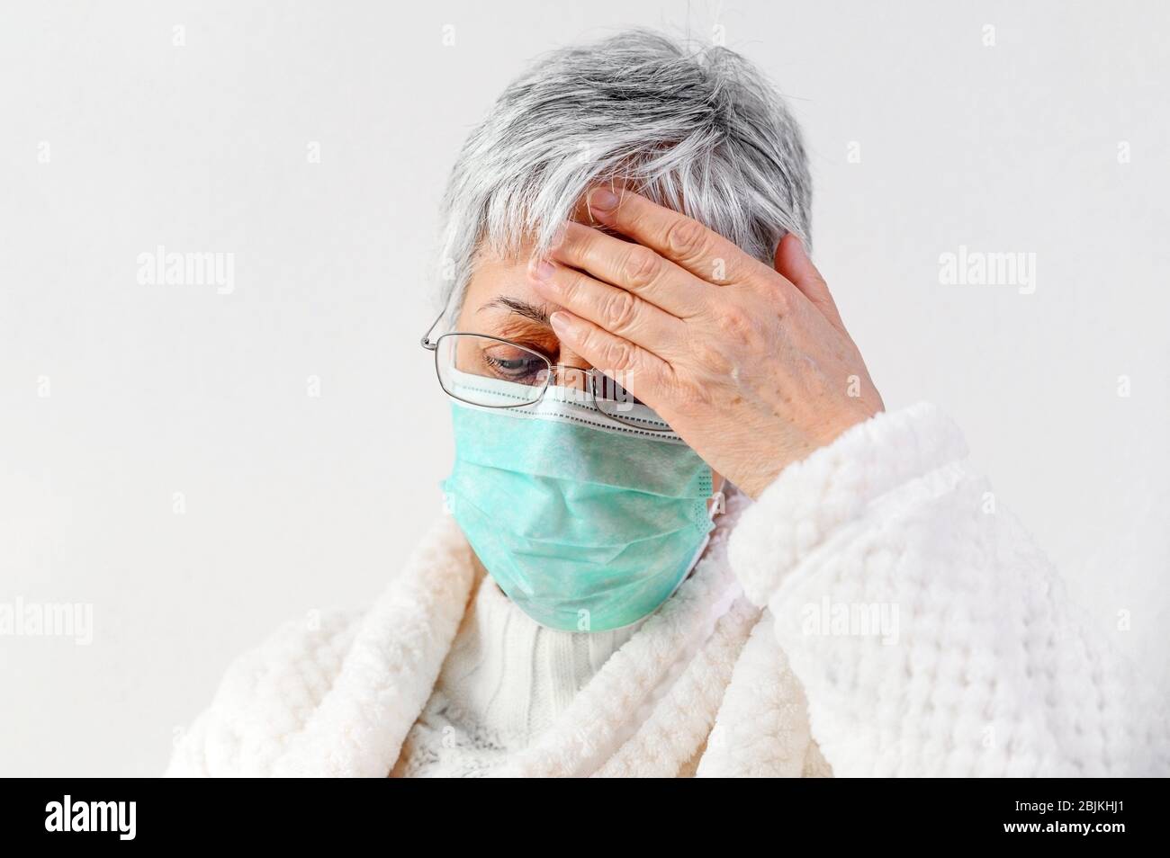 Covid-19. Sick senior woman portrait, wearing face protection mask, fever and coughing, pneumonia disease, risk patient, flu and cold. Stock Photo