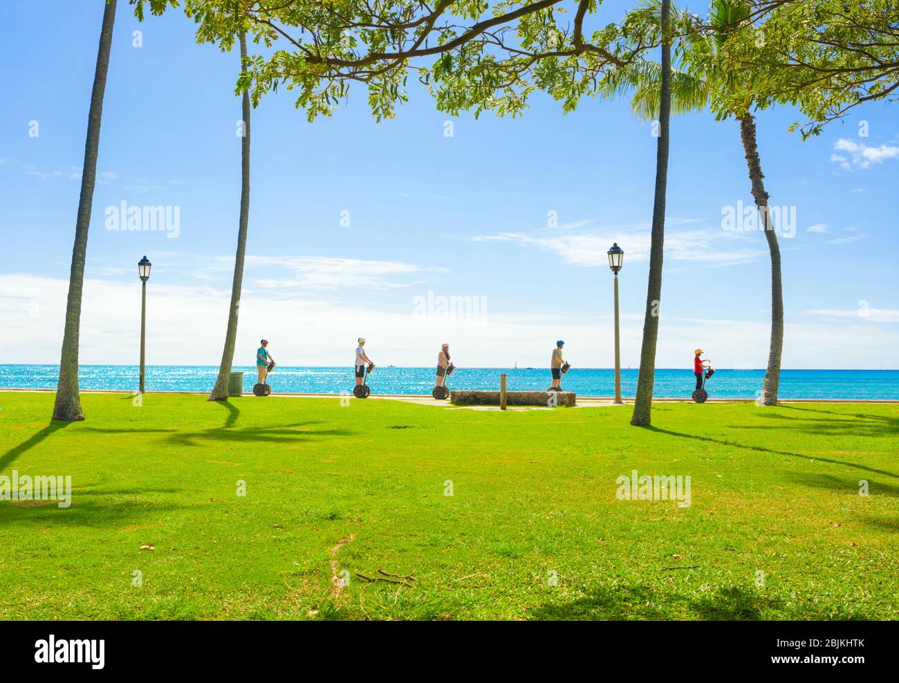 Group of five toursits riding self balancing scooters along the ocean walking path in Waikiki, Honolulu, Hawaii on bright sunny day Stock Photo